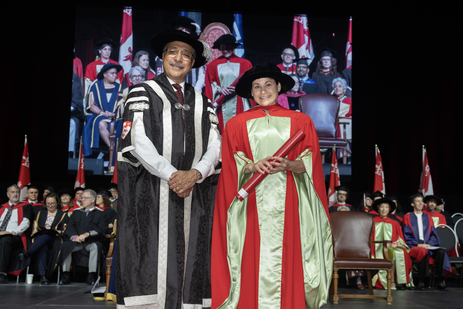 a man and a woman on a stage wearing convocation gowns and hats