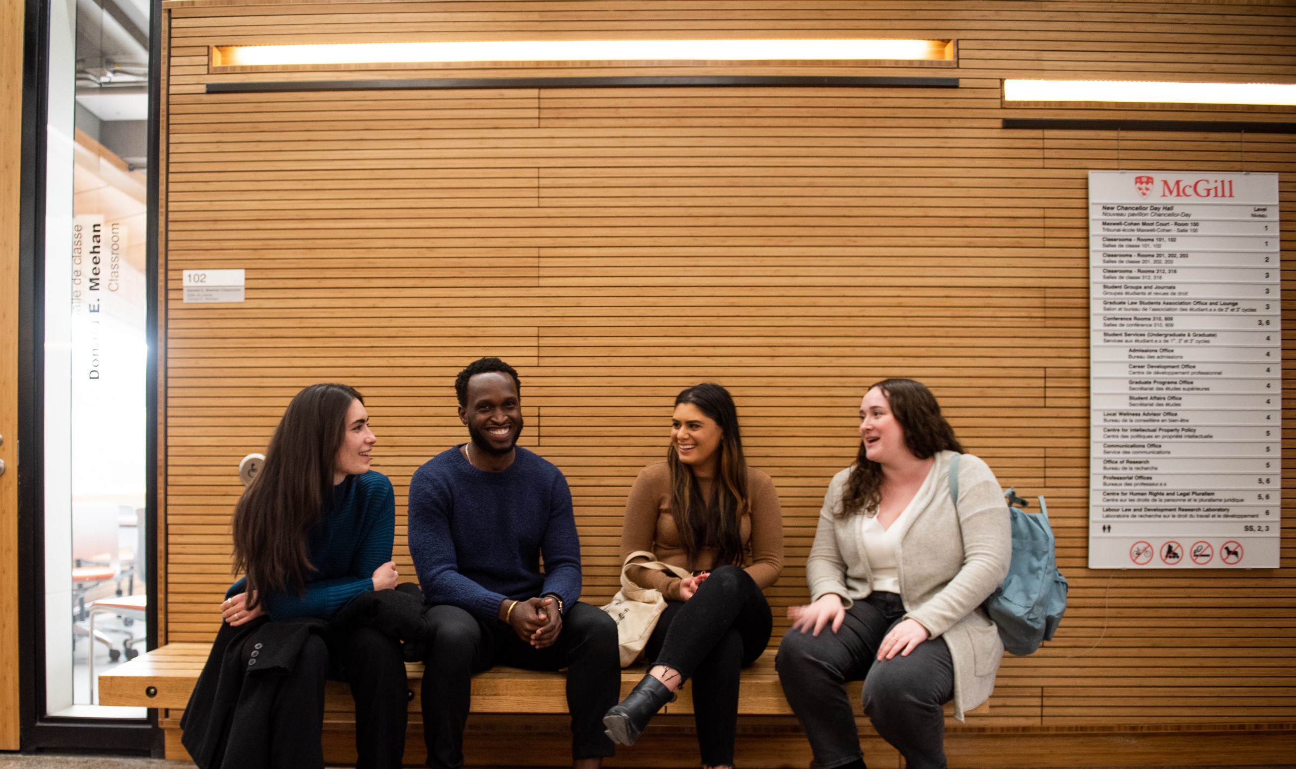 Three white female students and one black male student sitting on a bench discussing and smiling.