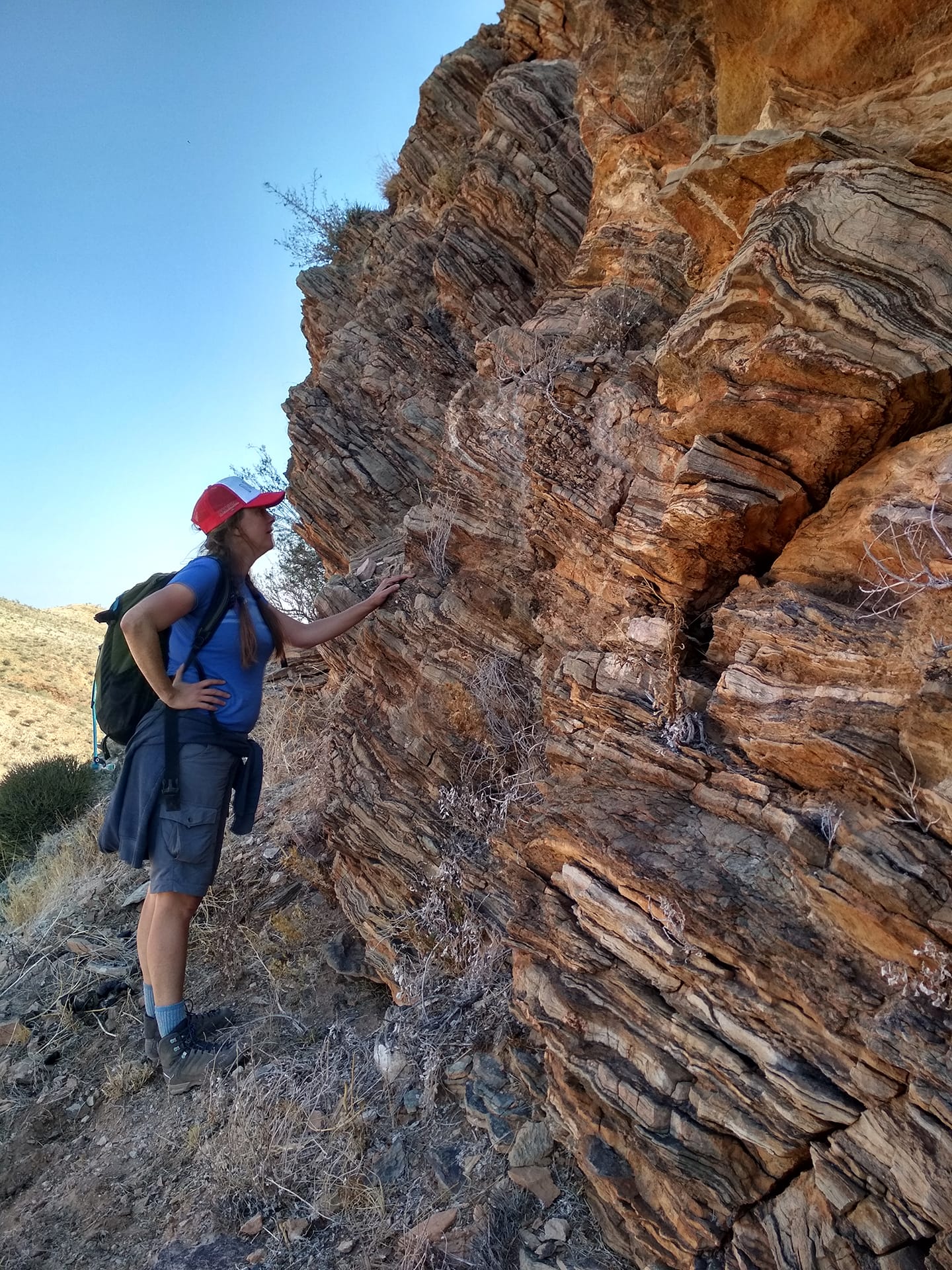 Professor Christie Rowe facing and touching a rock wall.