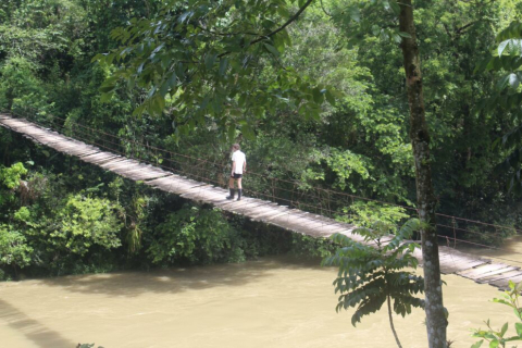 Benjamin Keenan crosses a simple suspension bridge over a river in Central America